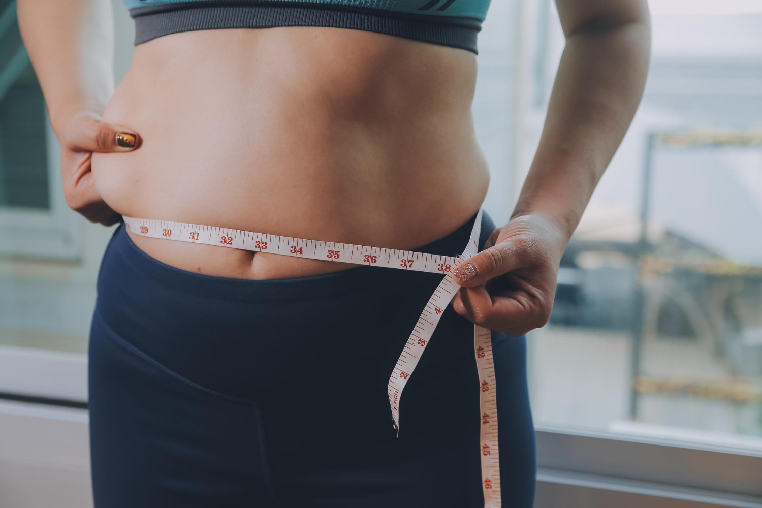 Nő fehér mérőszalaggal méri a hasát, mielőtt elkezdi az Eladó Adipex használatát a súlycsökkentéshez.